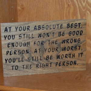 May include: Wooden sign with engraved text: "AT YOUR ABSOLUTE BEST, YOU STILL WON'T BE GOOD ENOUGH FOR THE WRONG PERSON. AT YOUR WORST, YOU'LL STILL BE WORTH IT TO THE RIGHT PERSON." The sign is on a wooden shelf.