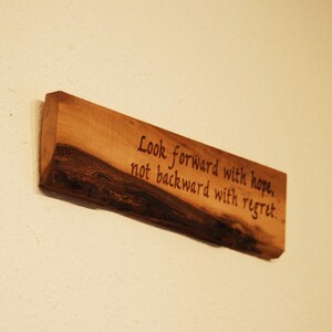 May include: A wooden sign with the text "Look forward with hope, not backward with regret." The sign is made of natural wood with a rustic finish.