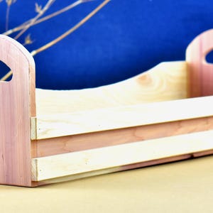 May include: A wooden box with two handles on the sides. The box is made of light brown wood and has a natural finish.