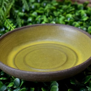 May include: A small, round, yellow ceramic bowl with a dark brown rim. The bowl is empty and has a slight sheen.