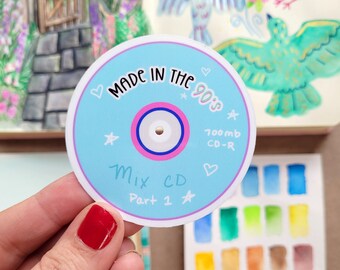 May include: A blue and pink sticker with a CD design. It says "Made in the 90's 700mb CD-R Mix CD Part 1" with stars and hearts around the text.