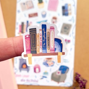 May include: A sticker featuring a bookshelf with colorful book spines. Titles include "The Housemaid," "The Women," "It Ends With Us," "The Nightingale," "Wicked," and "Little Women." The shelf is light brown with yellow supports, and the background includes other stickers.