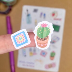 May include: Two stickers: a green cactus in a terracotta pot with a pink flower and a square sticker with a colorful floral design. The stickers are on a white background with other small illustrations.