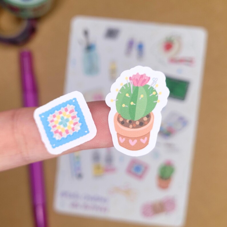 May include: Two stickers: a green cactus in a terracotta pot with a pink flower and a square sticker with a colorful floral design. The stickers are on a white background with other small illustrations.