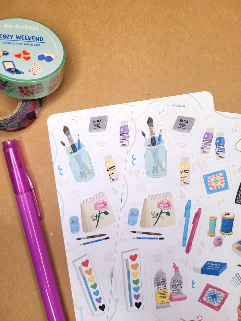 May include: A collection of art supplies and stationery items. Includes stickers with art-themed illustrations, washi tape with the text "COZY WEEKEND", a purple pen, and a variety of stickers featuring paintbrushes, paint tubes, and other art supplies.