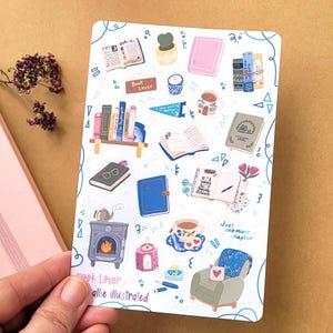 May include: A sticker sheet featuring illustrated elements related to reading and books. The stickers include open books, bookshelves, a cozy armchair, a teacup, and the text "Book Lover" and "Just one more chapter". The stickers are in various colors.