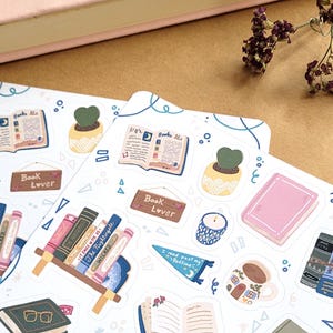 May include: A collection of stickers with a book theme. The stickers feature open books, stacks of books, potted plants, and the text "Book Lover". The color palette includes pink, blue, green, and brown.