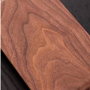Peut inclure: Gros plan sur une planche &agrave; d&eacute;couper rectangulaire en bois de couleur brun rouge&acirc;tre. Le grain du bois est pro&eacute;minent, affichant des motifs et des textures naturels. La surface de la planche est lisse, sugg&eacute;rant une finition de haute qualit&eacute;. Le fond sombre cr&eacute;e un contraste.