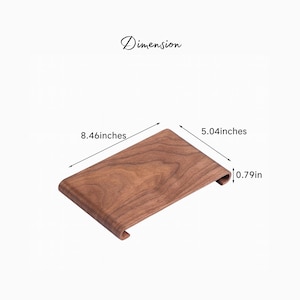 Peut inclure: Un support de t&eacute;l&eacute;phone en bois avec un design incurv&eacute;. Le support est marron avec un motif de grain de bois. Dimensions : 21,49 cm de long, 12,80 cm de large et 2,01 cm d'&eacute;paisseur. Le mot "Dimension" est &eacute;crit au-dessus.