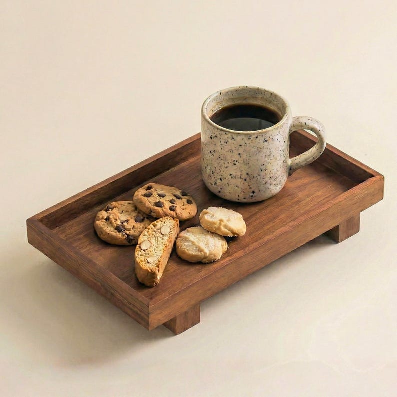 May include: A wooden serving tray holds a speckled ceramic mug filled with coffee and an assortment of cookies. The cookies include chocolate chip, biscotti, and shortbread, creating a cozy, inviting scene.
