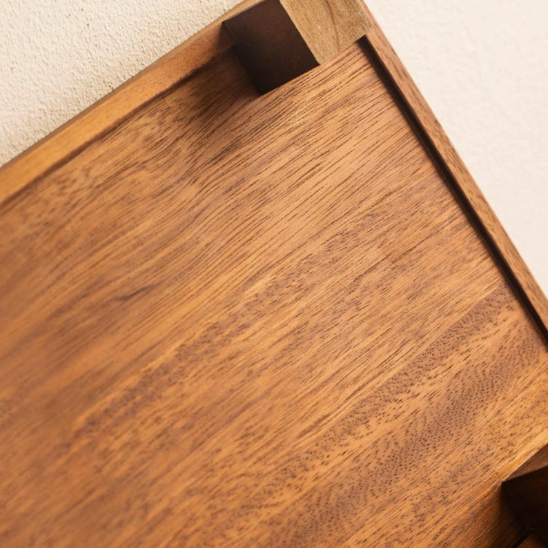 May include: Close-up of a wooden tray with a rich, warm brown color. The tray has a rectangular shape with a raised edge and a small, square wooden block at the corner. The wood grain is visible.
