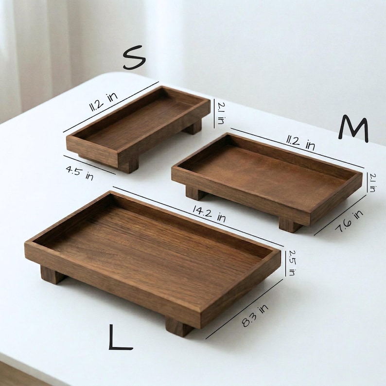 May include: Three wooden trays in varying sizes (S, M, L) are displayed. The trays are rectangular with raised edges and short, block-style feet. The smallest tray is 11.2 inches long, 4.5 inches wide, and 2.1 inches high. The medium tray is 11.2 inches long, 7.6 inches wide, and 2.1 inches high. The largest tray is 14.2 inches long, 8.3 inches wide, and 2.5 inches high.