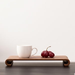 Peut inclure: Un plateau de service en bois avec un design incurv&eacute;, contenant une tasse blanche et une grappe de raisins rouges. Le plateau est en bois aux tons chauds et repose sur une surface sombre sur fond blanc.