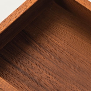 May include: Close-up of a wooden box with a rich, dark brown finish. The box has a square shape with visible wood grain, showcasing the natural texture and color variations of the material. The edges are neatly joined, indicating quality craftsmanship.