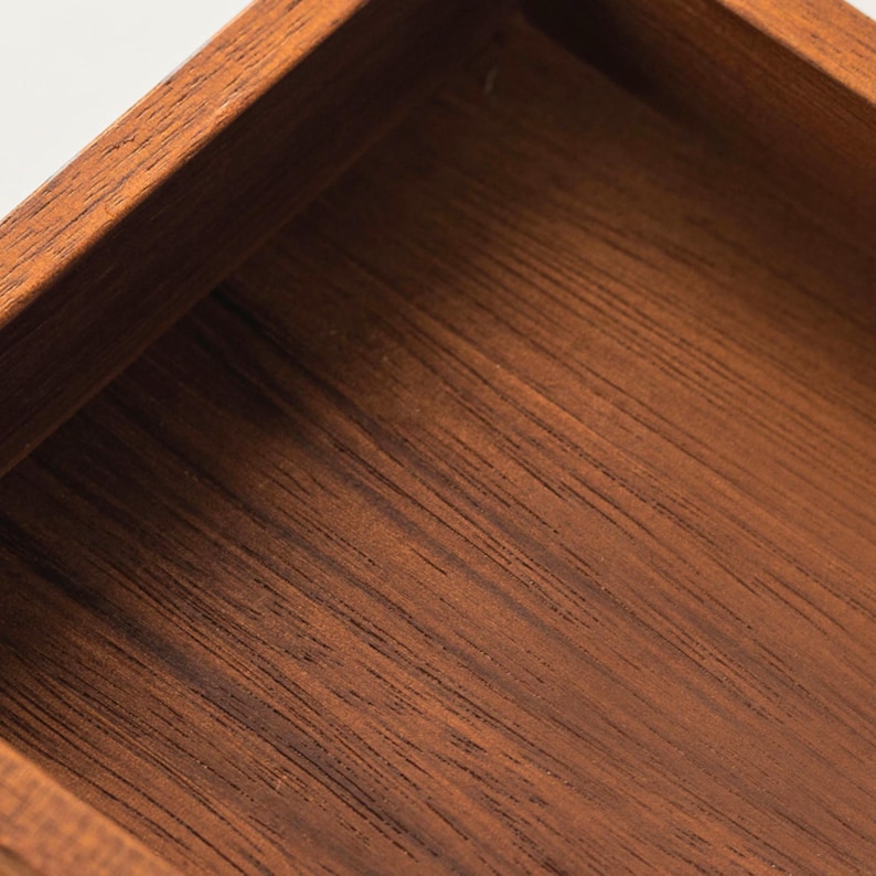 May include: Close-up of a wooden box with a rich, dark brown finish. The box has a square shape with visible wood grain, showcasing the natural texture and color variations of the material. The edges are neatly joined, indicating quality craftsmanship.