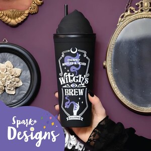 Puede incluir: Vaso reutilizable negro con tapa negra y una pajita. El vaso tiene un gr&aacute;fico de una mano de bruja morada sosteniendo una poci&oacute;n con el texto "Freshly Bottled & Hexed Witch's Brew" y una luna creciente y estrellas.