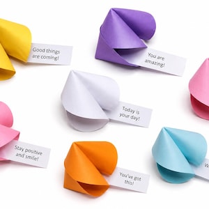 Op de afbeelding: Zeven kleurrijke papieren gelukskoekjes in geel, paars, roze, wit, oranje en lichtblauw. Elk koekje bevat een wit strookje papier met gedrukte tekst: Good things are coming, You are amazing, Today is your day, Believe in yourself, Stay positive and smile, You've got this en Wonderful things await you.