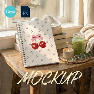 May include: A notebook with a cherry design, featuring two red cherries and a pink bow. The notebook is on a wooden table with a candle, a glass of green drink, and a stack of books. The word "MOCKUP" is at the bottom.