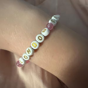 May include: A white beaded bracelet with pink beads and gold lettering spelling out "LONDON".