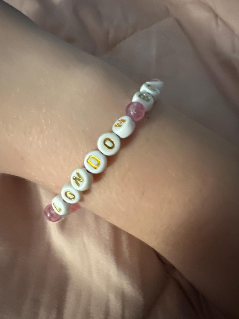 May include: A white beaded bracelet with pink beads and gold lettering spelling out "LONDON".