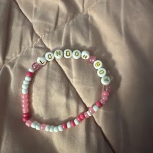 May include: A pink and white beaded bracelet with the words "LONDON BOY" spelled out in gold letters.