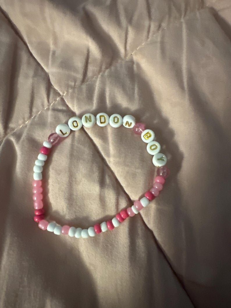 May include: A pink and white beaded bracelet with the words "LONDON BOY" spelled out in gold letters.