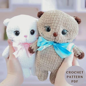 May include: Two plush crochet cat toys, one white with a pink satin bow and one light brown with dark brown ears and paws, featuring a bright blue satin bow. The text CROCHET PATTERN PDF is visible in the lower right corner of the image.