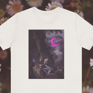 A super soft tshirt with a classic oil painting of a young man on one knee, bouquet of flowers in one hand while the other clutches the tree Lit by the light of the neon moon. A glowing pink neon moon with a few neon stars.