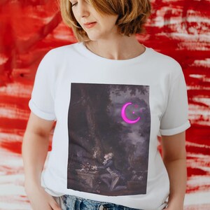 Może przedstawiać: Biały t-shirt z nadrukiem graficznym obrazu przedstawiającego p&oacute;łksiężyc i gwiazdy w r&oacute;żowym odcieniu. Obraz jest umieszczony na tle ciemnego lasu.