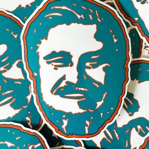 May include: A stack of teal and orange stickers featuring a stylized portrait of a man with a beard. The stickers are circular and have a white background.