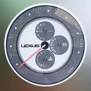 May include: A circular Lexus car dashboard gauge with a speedometer, fuel gauge, and other indicators. The speedometer displays MPH and km/h. The gauge has a white face with black and gray accents and the Lexus logo.