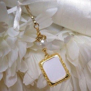 May include: Gold bookmark with a white pearl and a square frame with a blank white space inside. The bookmark is on a white background.