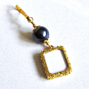 May include: A gold-tone charm with a black pearl and a small gold picture frame.