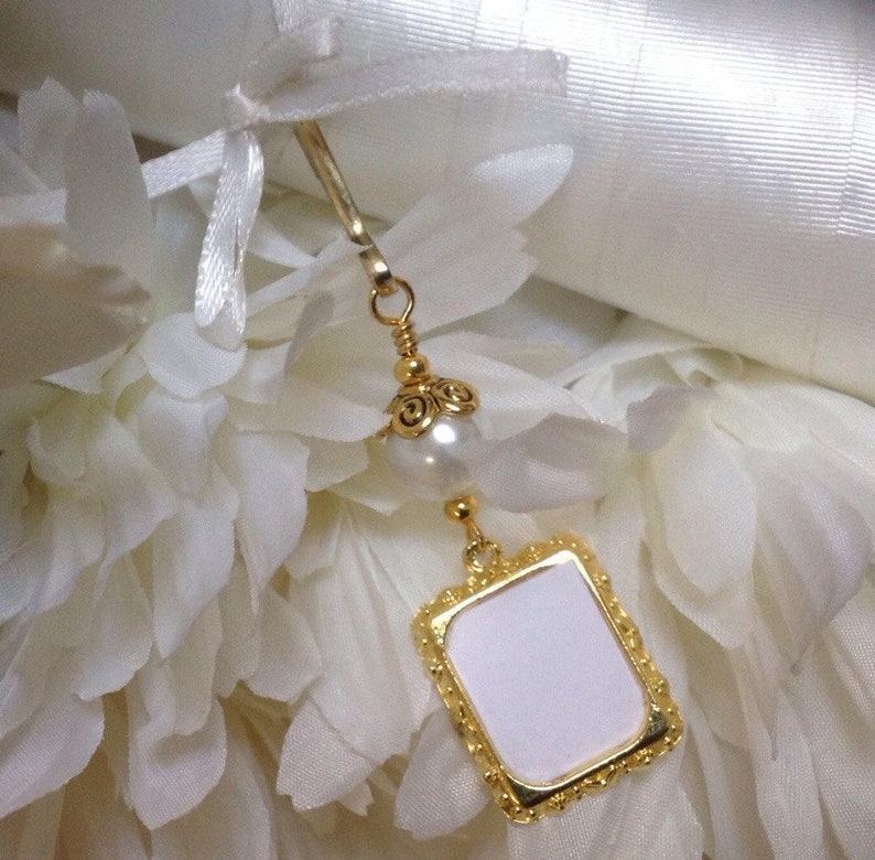 May include: Gold bookmark with a white pearl and a square frame with a blank white space inside. The bookmark is on a white background.