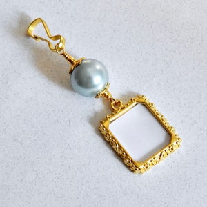May include: A gold-toned picture frame charm with a gray pearl bead and a gold-toned clasp.