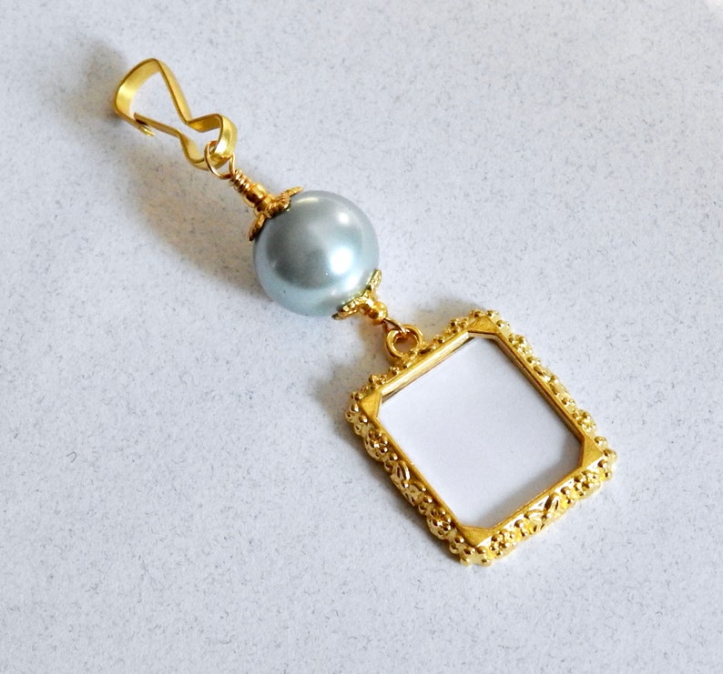 May include: A gold-toned picture frame charm with a gray pearl bead and a gold-toned clasp.