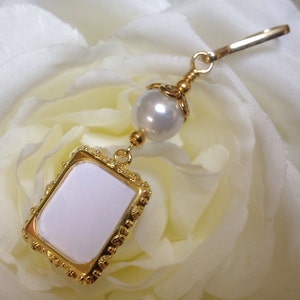 May include: A gold-toned charm with a white pearl and a small, white, rectangular frame with a gold border.