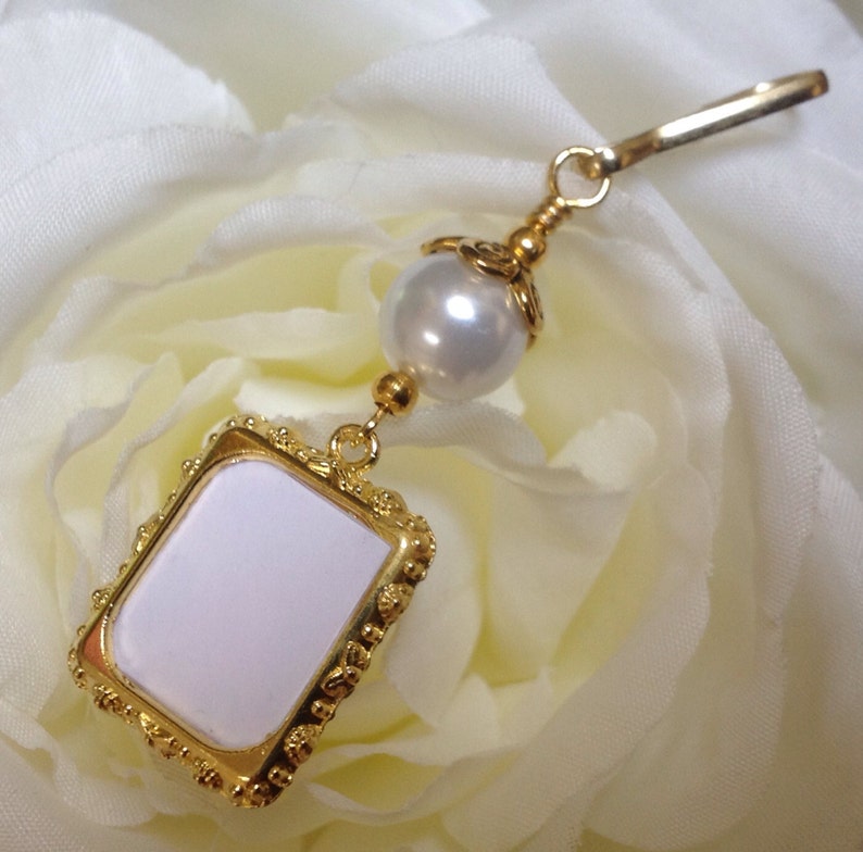 May include: A gold-toned charm with a white pearl and a small, white, rectangular frame with a gold border.