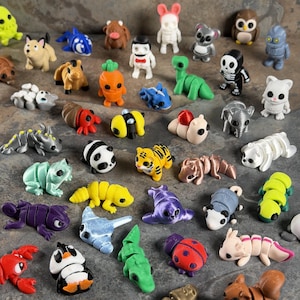 Może przedstawiać: Kolekcja kolorowych, małych figurek w różnych wzorach zwierząt i postaci. Figurki obejmują m.in. pandę, tygrysa, sowę i szkielet. Figurki są wykonane z tworzywa sztucznego i ułożone na teksturowanej powierzchni.