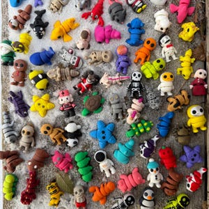 Pode incluir: Uma coleção de figuras em miniatura coloridas de várias formas, incluindo animais, pessoas e formas abstratas. As figuras são em tons de amarelo, azul, rosa, verde e laranja, com alguns detalhes intrincados.