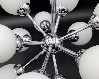 Puede incluir: Una lámpara de araña estilo sputnik con una esfera central cromada y múltiples brazos radiantes. Cada brazo termina en un globo esférico de vidrio blanco esmerilado. La lámpara está construida con componentes de metal cromado pulido.