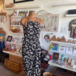 Könnte beinhalten: Ein schwarz-weißer Jumpsuit mit Muster auf einer Schaufensterpuppe. Das Neckholder-Top und die Wickelhose haben ein sich wiederholendes abstraktes Design. Der Jumpsuit befindet sich in einem Geschäft, umgeben von Regalen mit Schmuck und Kunst.