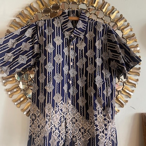 Może przedstawiać: Koszula z krótkim rękawem zapinana na guziki z geometrycznym wzorem w kolorze złotym i granatowym. Wzór to powtarzający się wzór diamentów i linii.