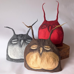 May include: Three felt owl-shaped tea cozies in red, gray, and brown. The owls have closed eyes and long, thin ears.