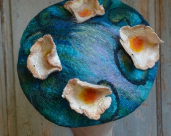 May include: A blue felt beret with white felt flowers and orange centers. The flowers are arranged around the hat in a circular pattern.