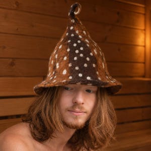 May include: A conical felted hat featuring a brown and dark brown mottled pattern with scattered white polka dots. The hat has a wide, slightly flared brim and a distinct, curled pointed top, crafted from a textured, dense wool-like material.