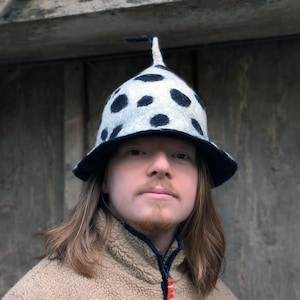 Peut inclure: Un chapeau fantaisiste avec une base blanche et des pois noirs. Le chapeau a un large bord bleu foncé et un petit accent noir vertical. Un accessoire unique.