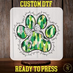 May include: A green, gold, and white paw print with a black and white bow. The paw print is surrounded by the text "Happy St. Patrick's Day".