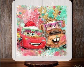 May include: A square, white sublimation transfer featuring Lightning McQueen and Mater from the Cars movie, both wearing Christmas accessories. The background has a watercolor effect with red, green, and pink splashes. Text at the top reads "CUSTOM DTF" and at the bottom "READY TO PRESS".