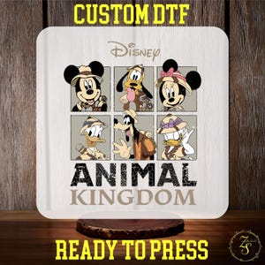 May include: A white sublimation blank with a design featuring Disney characters Mickey Mouse, Minnie Mouse, Donald Duck, Goofy, and Pluto in safari outfits. The design includes the text "Disney Animal Kingdom" and is ready to press.
